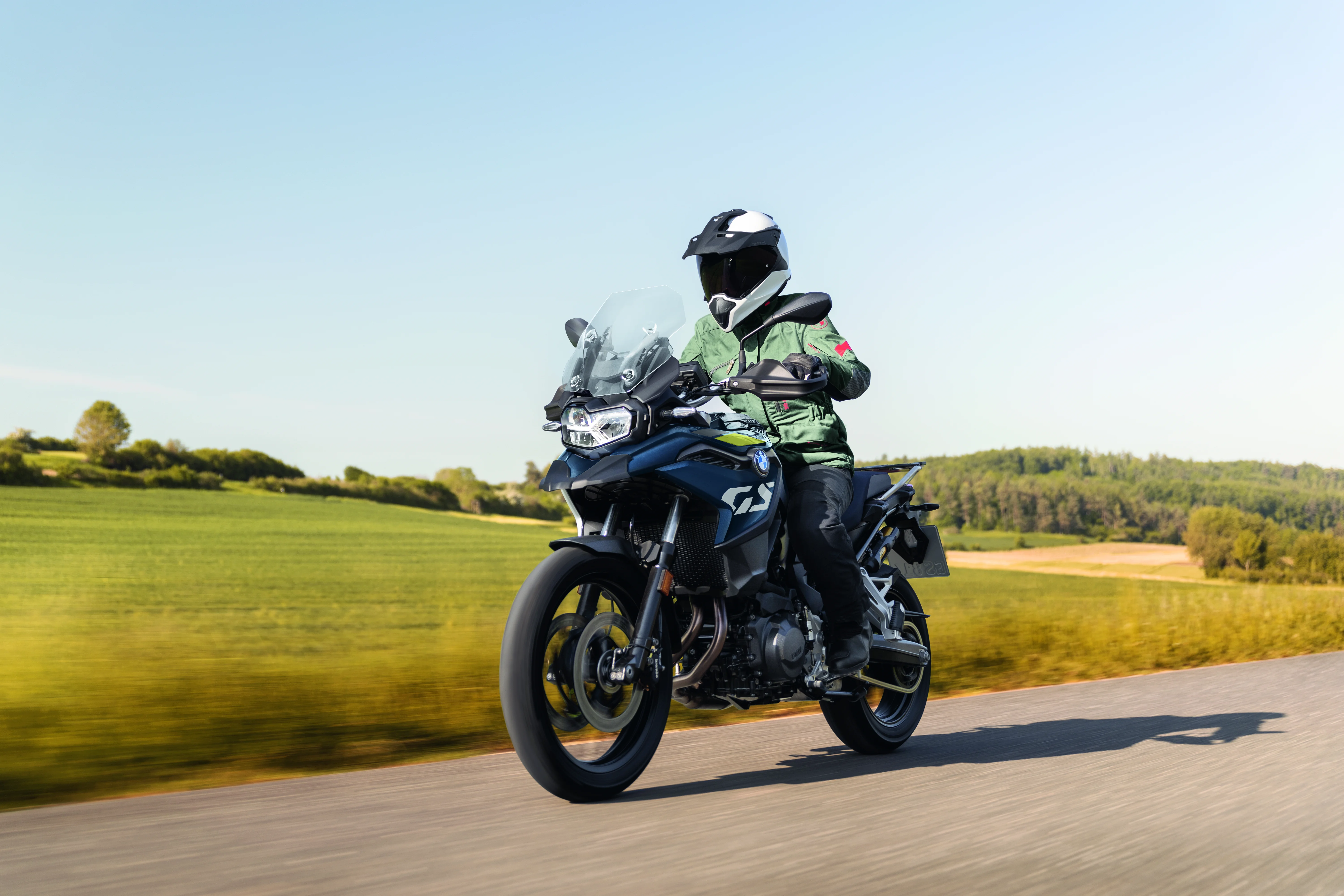 2026 BMW F 800 GS riding on a rural road with fields and a bright sky in the background.